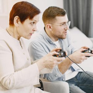 A senior and young adult playing video games together in a cozy living room setting.