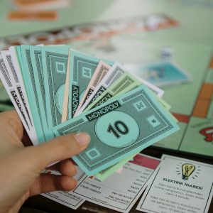 Hand holding colorful Monopoly money over a game board, symbolizing strategy and play.