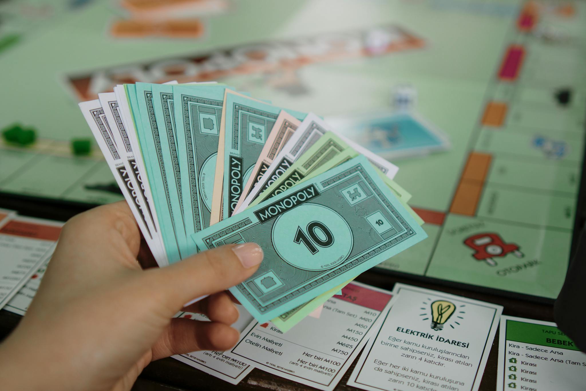 Hand holding colorful Monopoly money over a game board, symbolizing strategy and play.