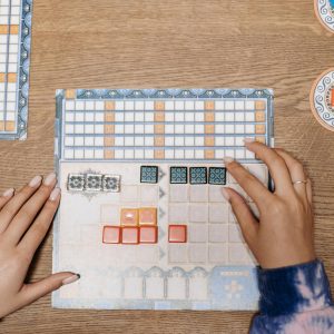 Hands arranging tiles on a strategic board game during a fun game night.
