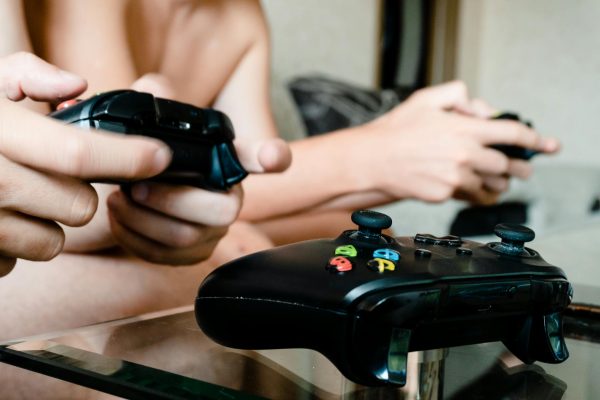 Two people playing video games with controllers on a glass table indoors.